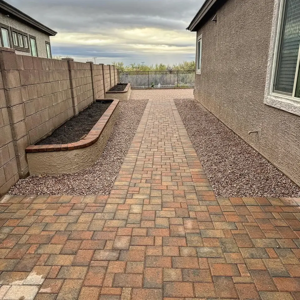 Paver walk between gravel beds, with a raised planter along the wall.