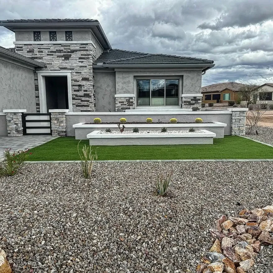 Front yard with artificial turf, a raised planter of barrel cacti, and gravel.