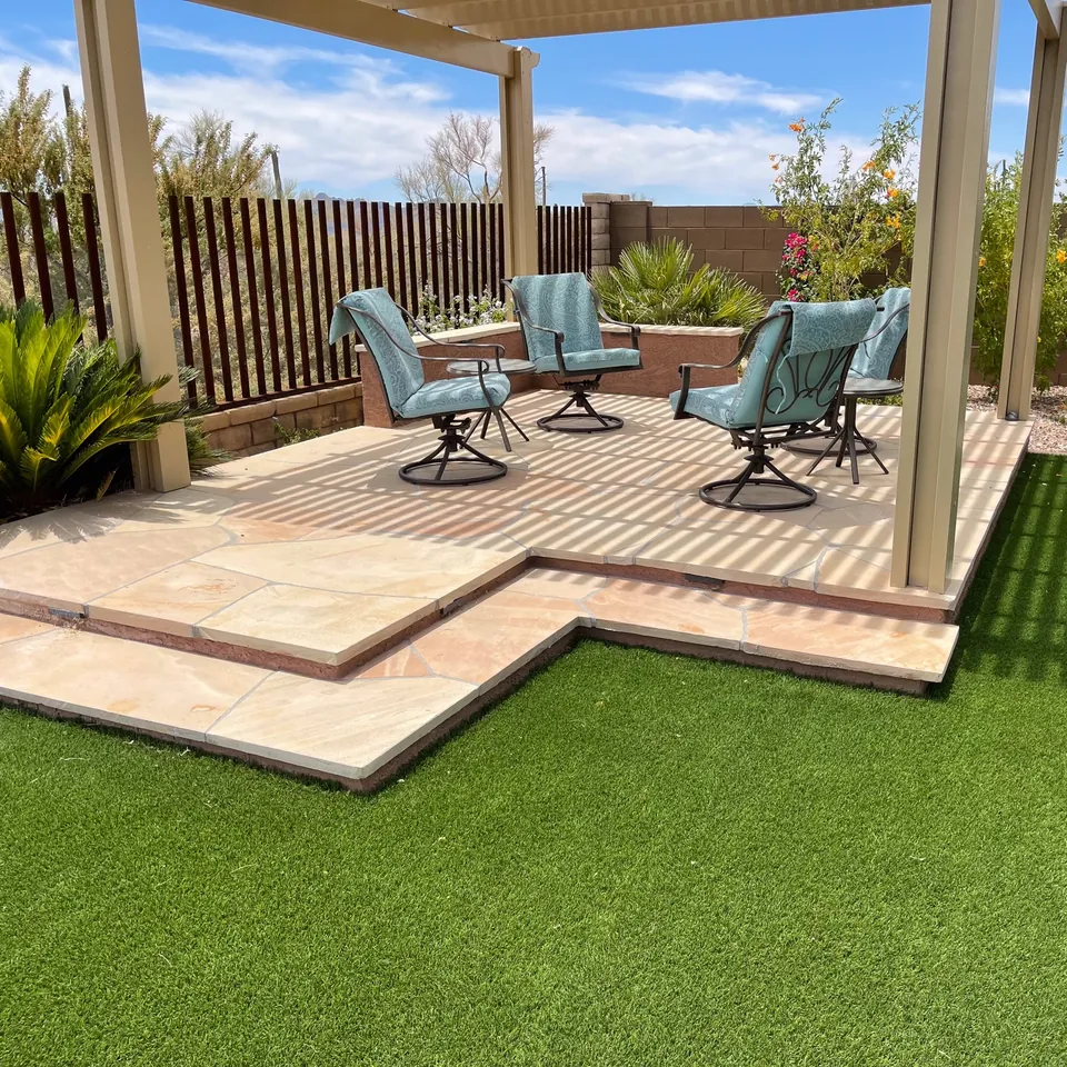 Artificial turf beside an irregular stone patio under a shade structure.