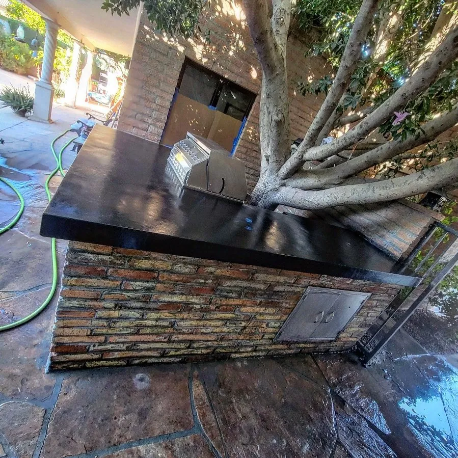 Brick outdoor kitchen with a black countertop and a stainless side burner.