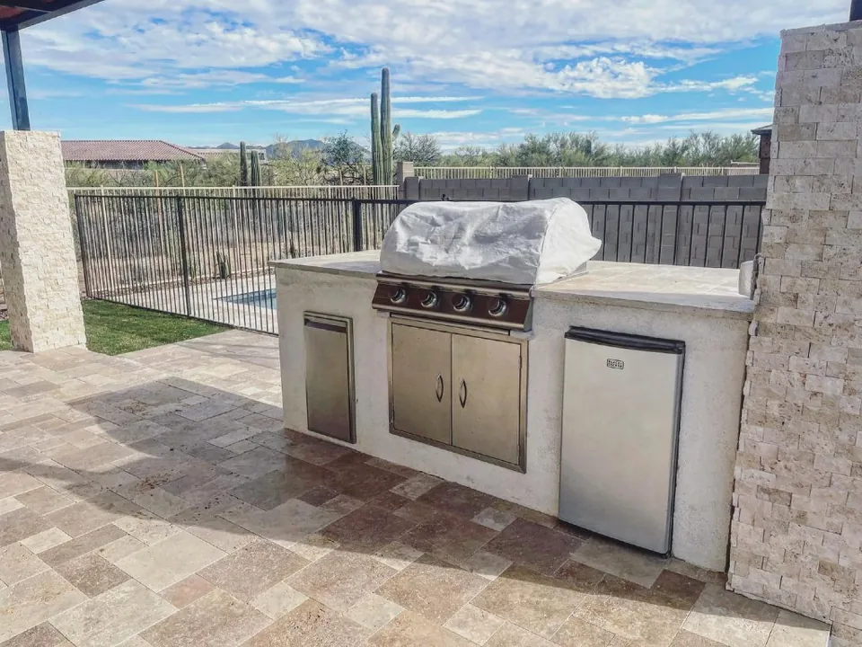 Built-in outdoor grill and refrigerator on a light stone paver patio.