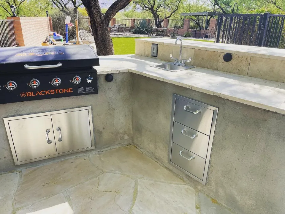 Built-in griddle, sink, and stainless storage on a stucco outdoor kitchen.