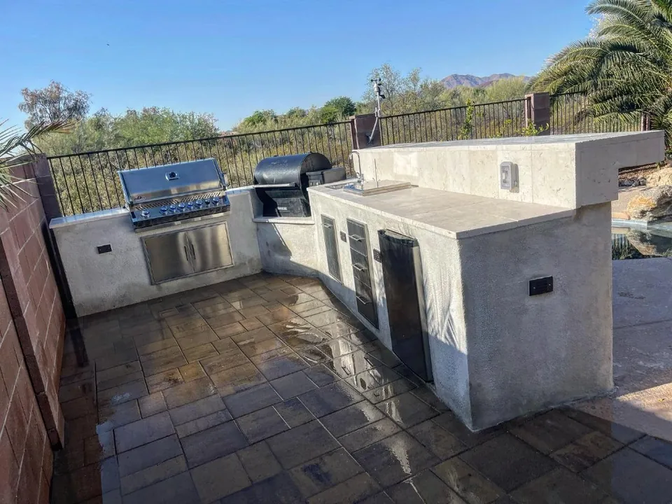 L-shaped outdoor kitchen with a built-in grill, smoker, sink, and refrigerator.