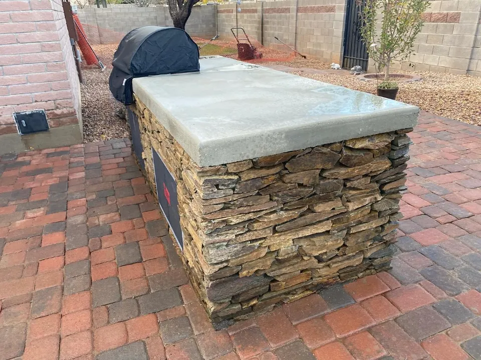 Stacked-stone outdoor kitchen with a concrete counter on a brick paver patio.