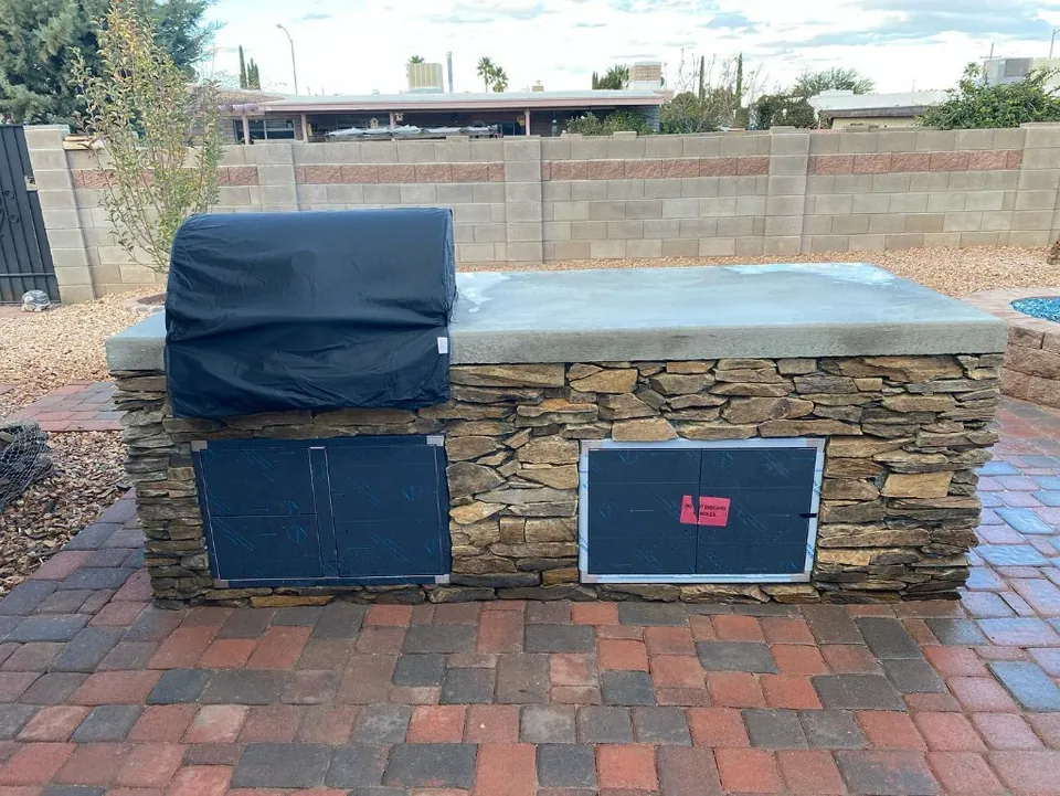 Stacked-stone outdoor kitchen with a concrete countertop and a covered built-in grill.