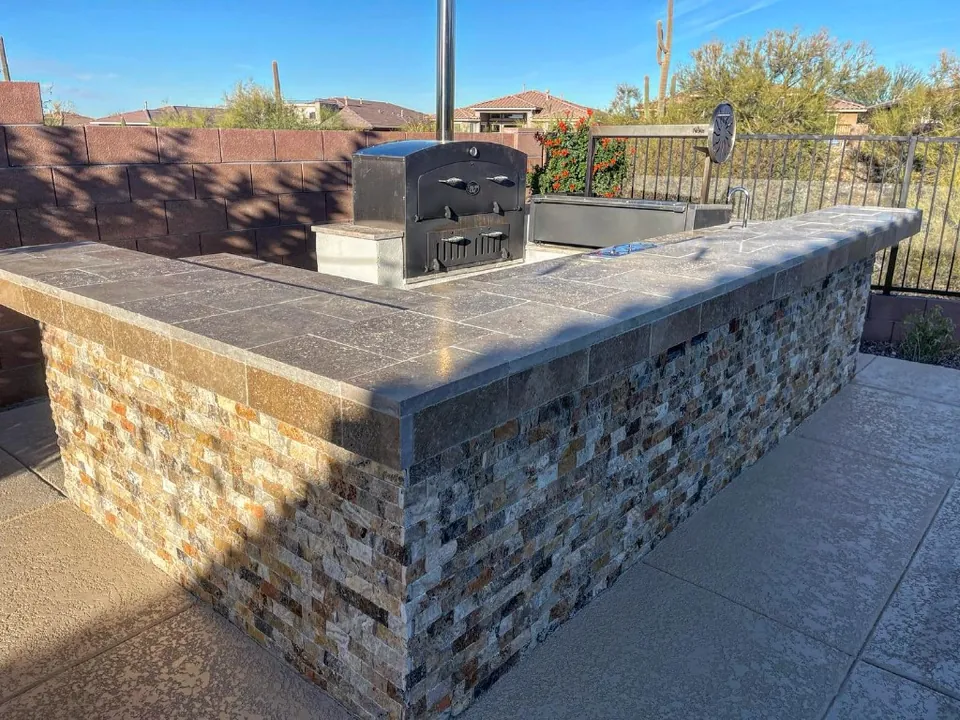 Stacked-stone outdoor kitchen with a wood-fired oven and sink.