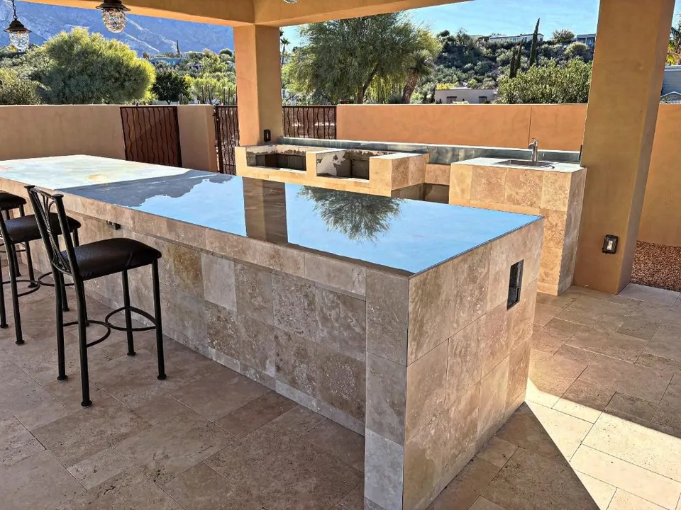 Stone-tile outdoor kitchen bar with seating and a cooking counter behind it.