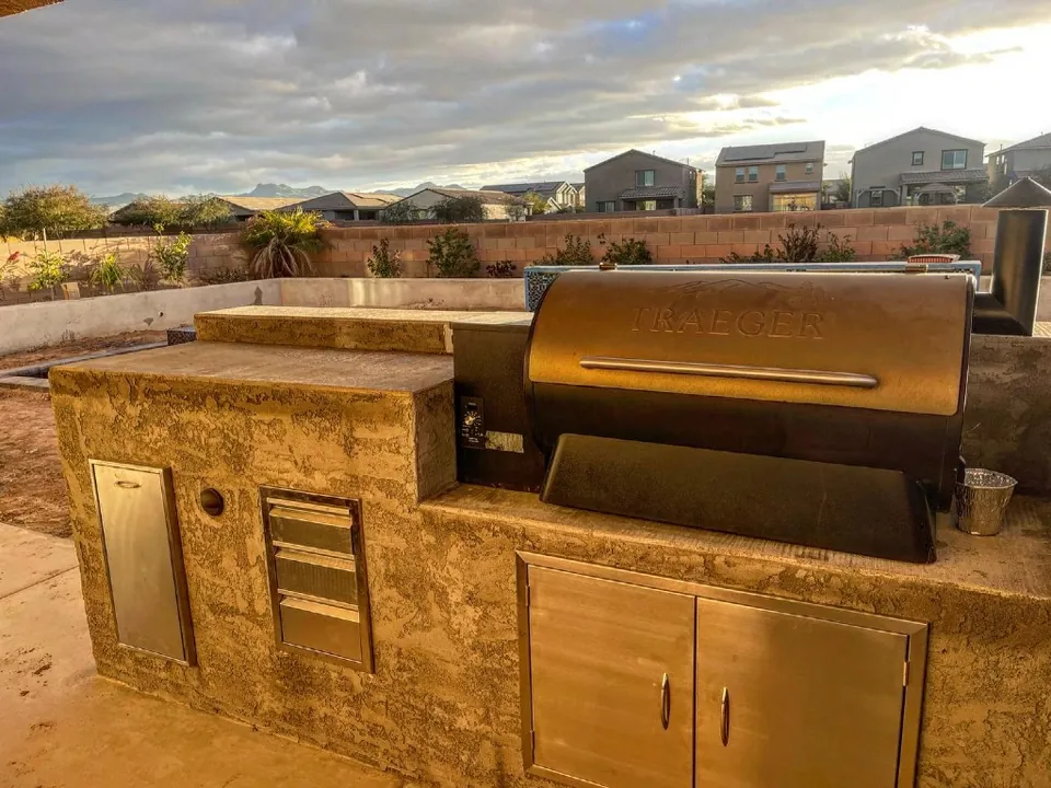 Stucco outdoor kitchen with a built-in pellet grill and stainless cabinets.